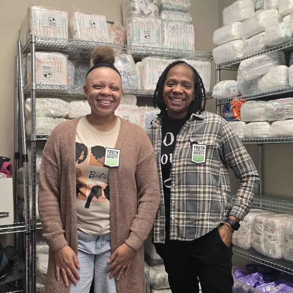 Two people stand smiling in a room with many supplies